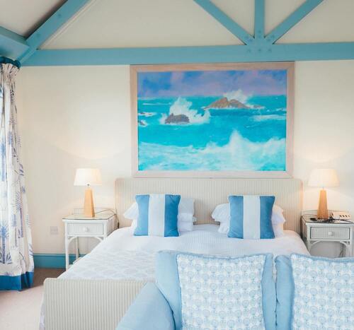 Chambre lumineuse de couleurs blanc et bleu, lit double avec un grand tableau de vagues au dessus de la tête de lit