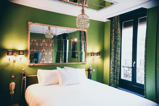 Chambre lit double, mirroir au dessus de la tête de lit et au plafond, lustre et ferronerie cuivrés, grande fenêtre sur rue