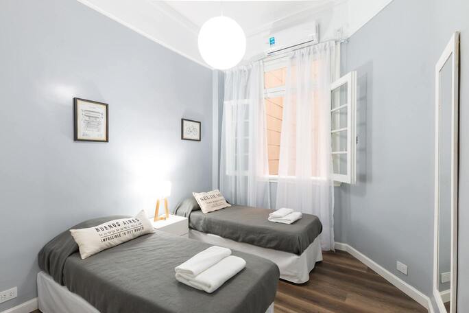 Chambre couleur clair avec deux lits une place et une fenêtre